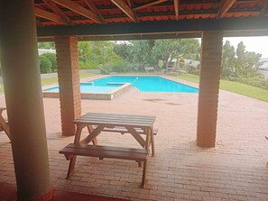 Un espacio al aire libre techado con piscina, mesa de picnic y suelo de ladrillo.