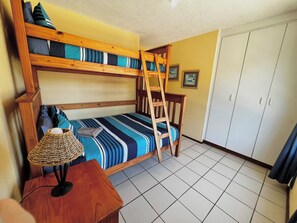 A bunk bed room with a ladder, a small table with a lamp, and a wardrobe.