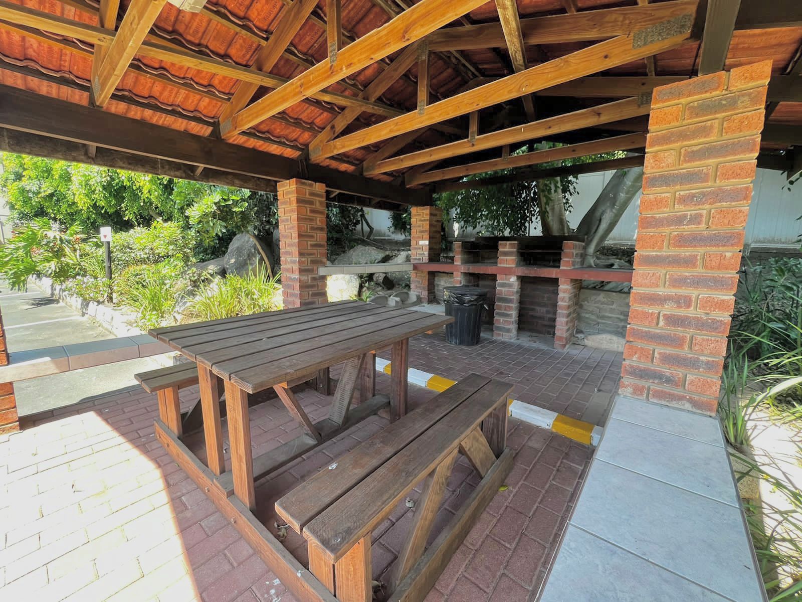 Eine Terrasse im Freien mit einem Holztisch und Bänken, Ziegelstützen und einem gefliesten Boden.