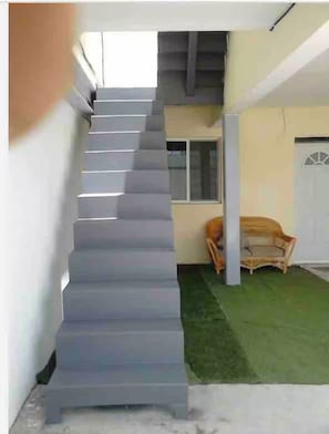 Eine Treppe führt zu einer zweiten Etage, im Hintergrund steht ein Stuhl und eine Tür.