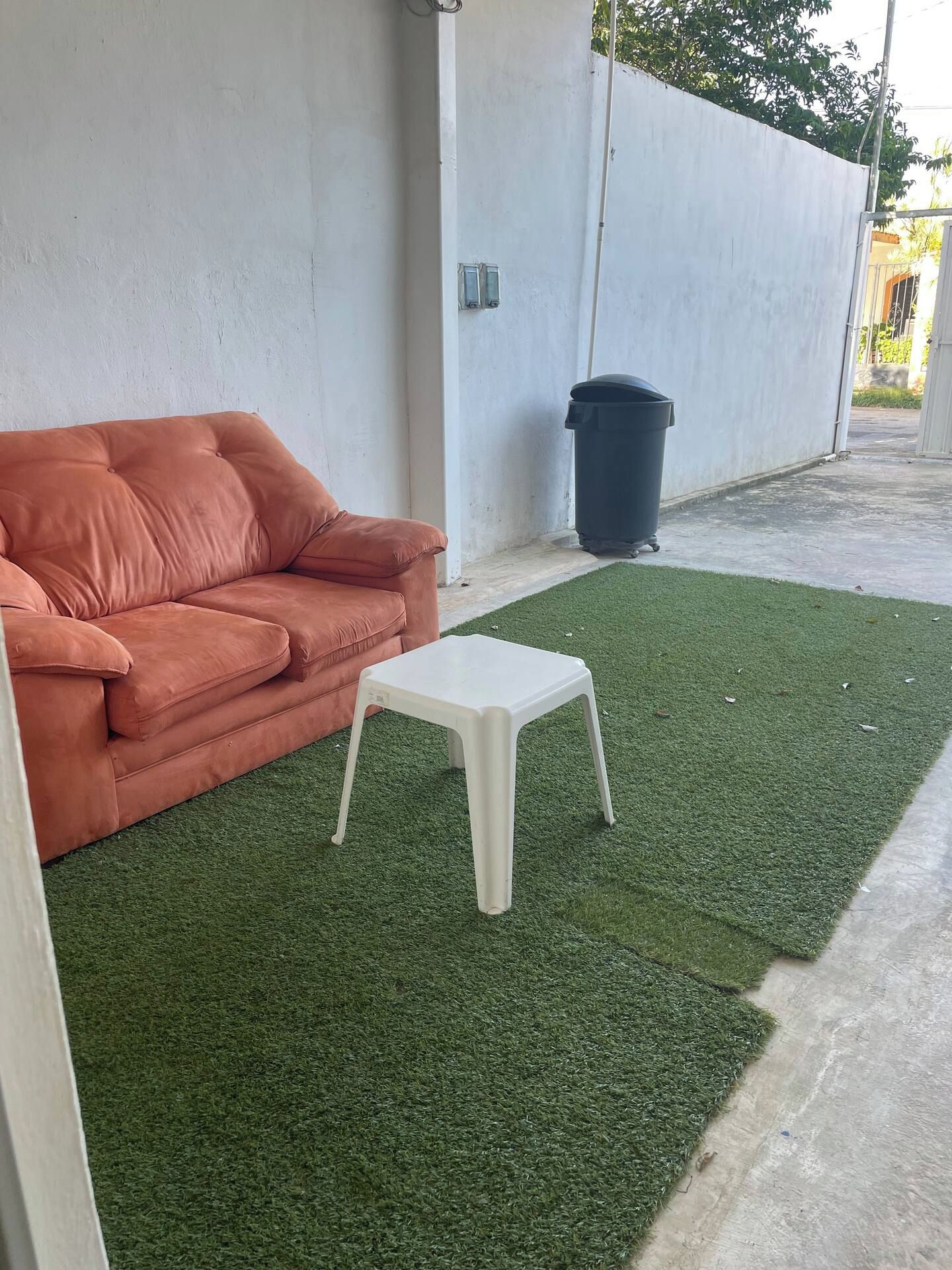 A room with a sofa and a small white table on a green artificial turf.