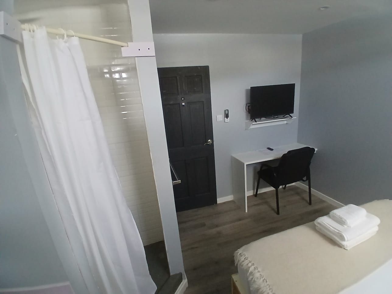 A hotel room with a bed, a desk, a chair, a television, and a door.