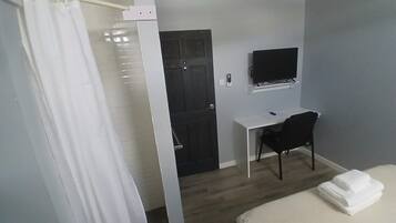 A hotel room with a bed, a desk, a chair, a television, and a door.