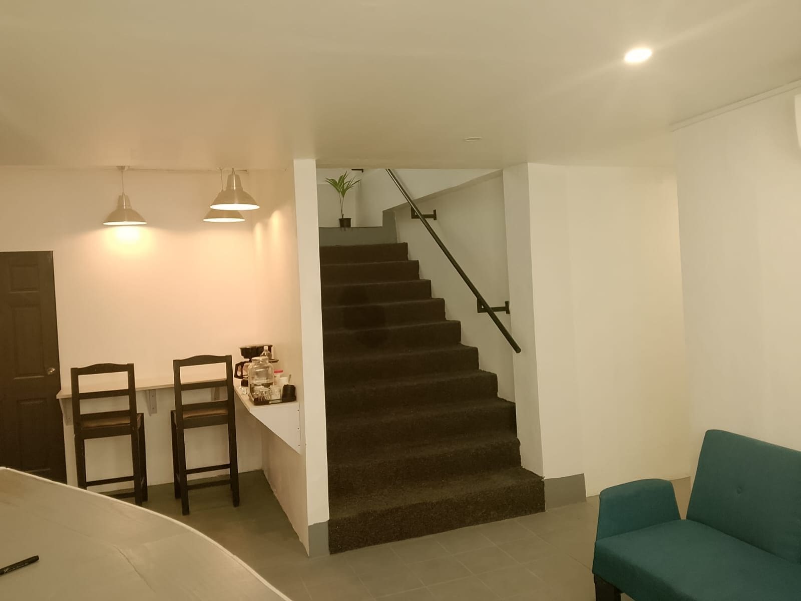 A staircase leading to an upper floor, a dining area with chairs and a table, and a teal sofa in the living area.