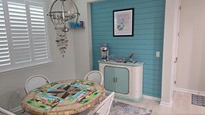 A dining area with a round table, wicker chairs, a teal accent wall, a chandelier, and a cabinet with decorative items. - Marvelous 2-bedroom condo with upgraded amenities in Margaritaville Hilton Head. (Hardeeville)