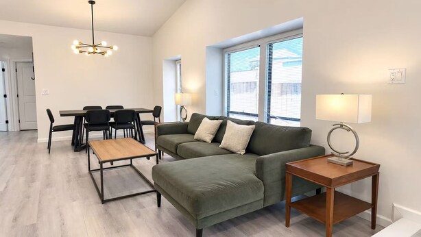 A modern living room with a sectional sofa, a coffee table, a dining table with chairs, and a lamp.