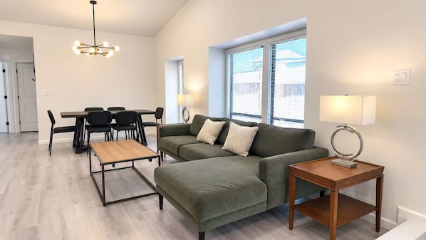 A modern living room with a sectional sofa, a coffee table, a dining table with chairs, and a lamp.