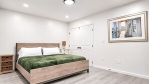 A bedroom with a bed, bedside table, nightstand, and a framed picture on the wall.