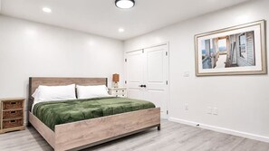 A bedroom with a bed, a nightstand, a dresser, a door, and a framed picture on the wall.