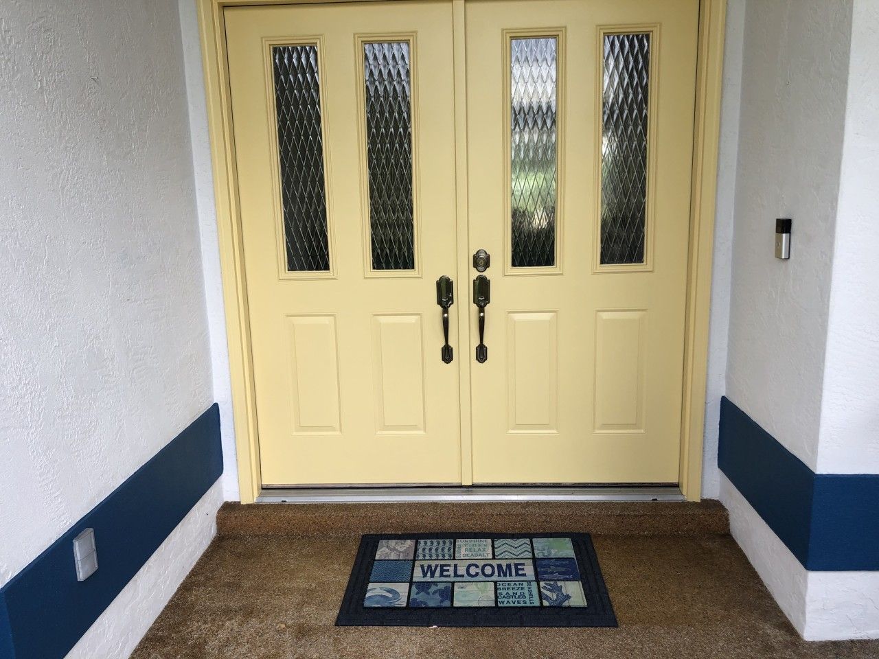 A yellow double door with a welcome mat in front.