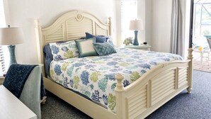 A bed with a floral bedspread, a bedside table with a lamp, and a view of the outdoors through a window. - Gulf Tranquility in Rotonda West (Rotonda West)