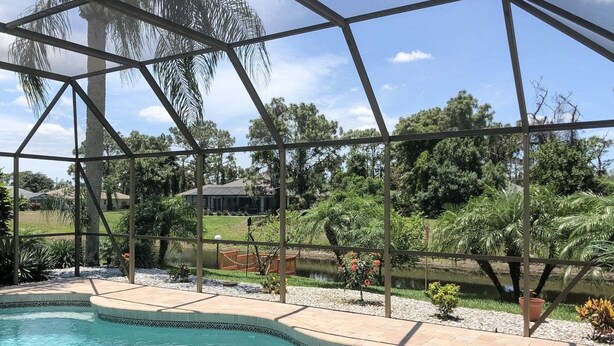 A swimming pool with a clear view of the surrounding landscape, including trees and a distant building. - Gulf Tranquility in Rotonda West (Rotonda West)