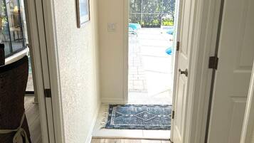 A hallway with a wooden floor leading to a door, a rug, and a framed picture on the wall.