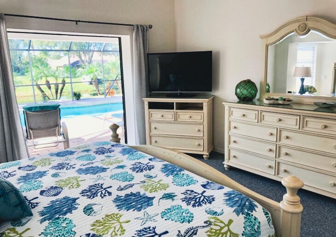 Une chambre à coucher avec un lit, une télévision, une commode et une vue sur une piscine.