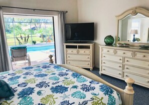A bedroom with a bed, a television, a dresser, and a view of a swimming pool.