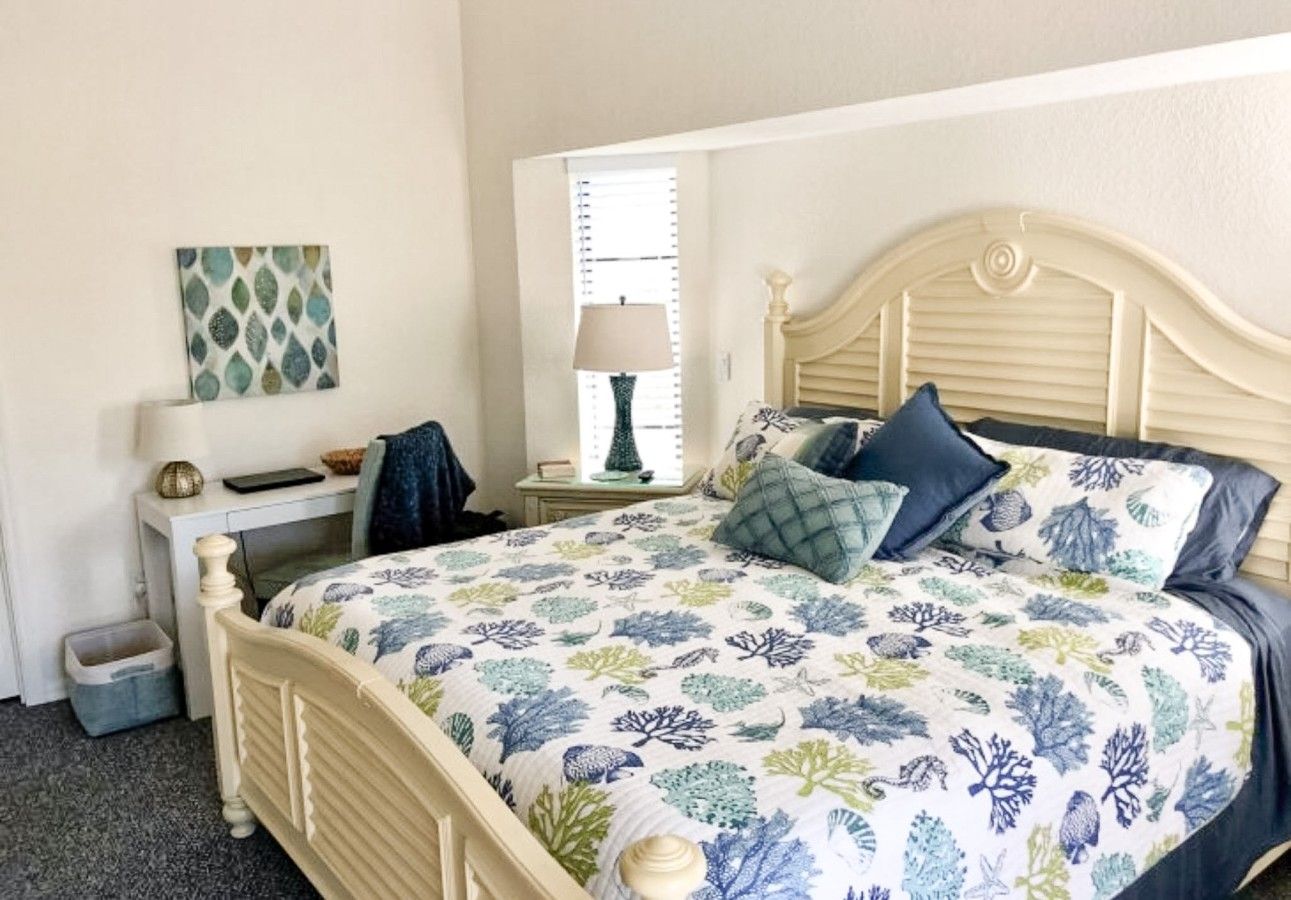A bedroom with a bed, bedside tables, a lamp, a window, and a wall decoration.