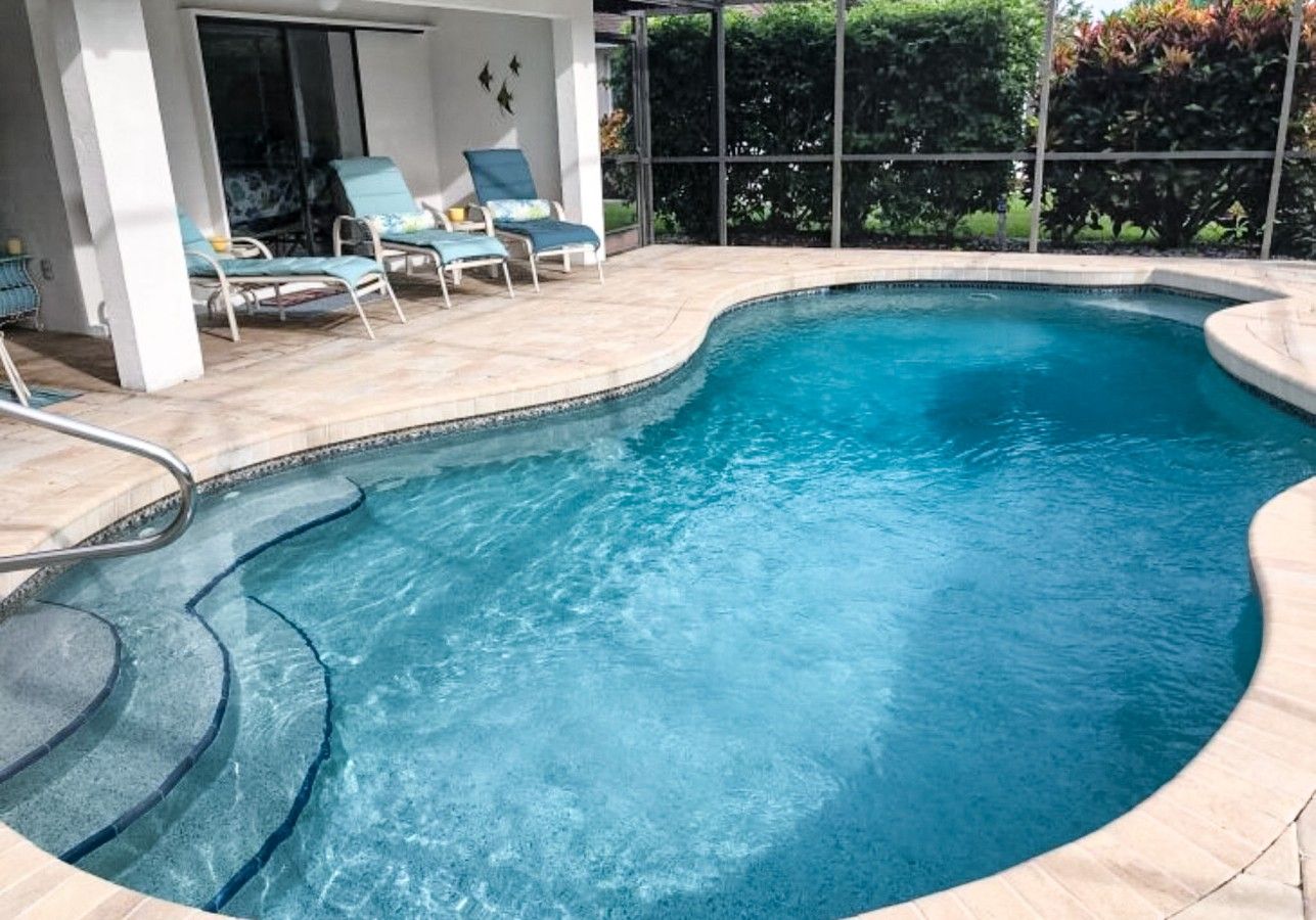 A swimming pool with a curved edge, a small deck area with lounge chairs, and a glass enclosure in the background.