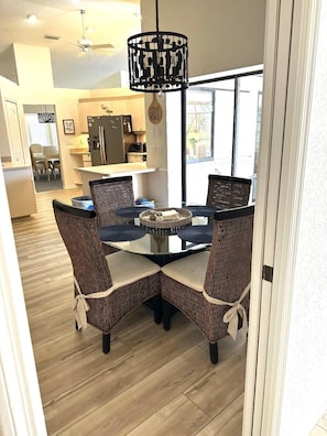 A dining area with a glass-top table, wicker chairs, and a black pendant light.