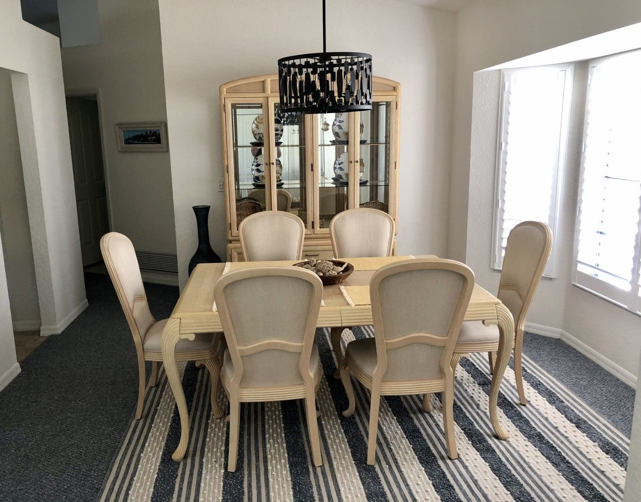 A dining room with a round table, six chairs, a chandelier, and a glass-fronted cabinet.