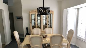 A dining room with a round table, six chairs, a chandelier, and a glass-fronted cabinet.
