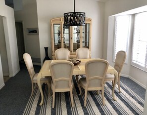 Un comedor con una mesa redonda, seis sillas, una araña y un aparador con puertas de vidrio.