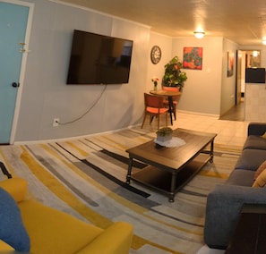 Un salon avec un téléviseur à écran plat fixé au mur, une table basse, un canapé et un tapis à rayures.