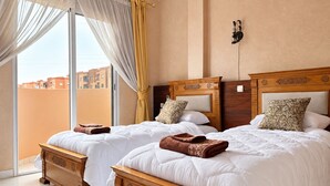 Habitació d'hotel amb dos llits, una finestra gran amb cortines, vista a edificis a l'exterior i una làmpada penjant de la paret.