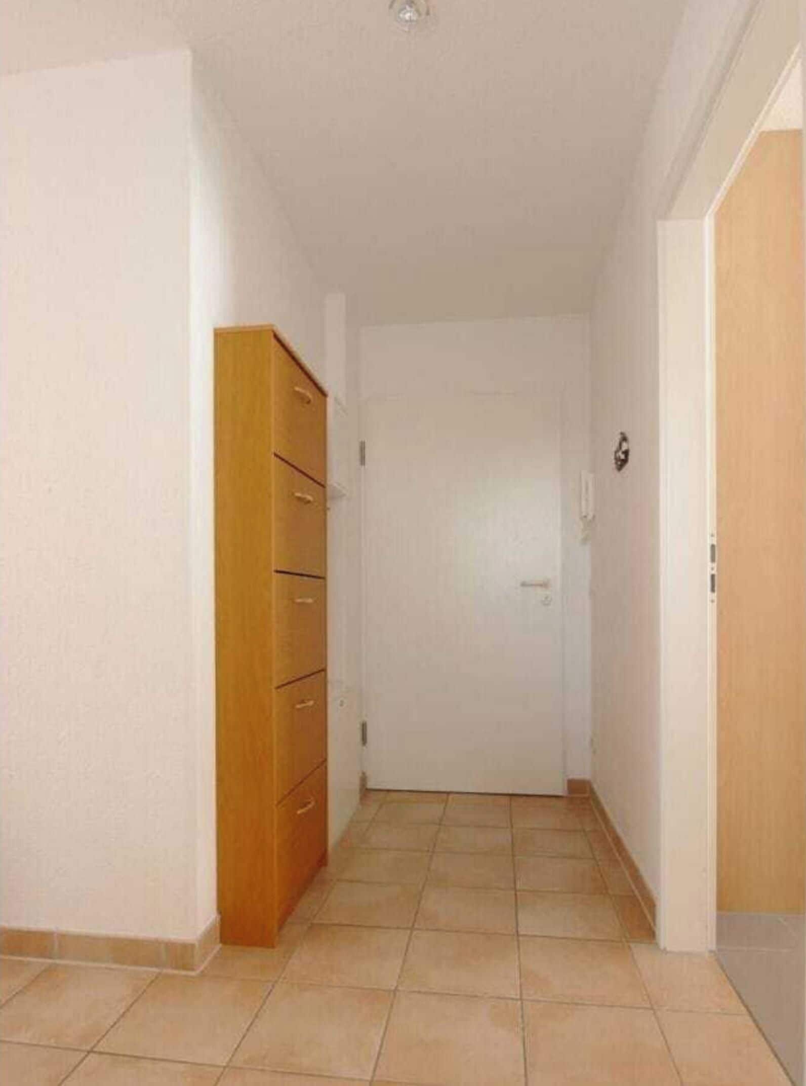 Ein Flur mit einem Holzschrank, einer weißen Tür und Fliesenböden.