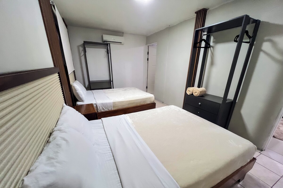 A hotel room with two beds, a wardrobe, a mirror, and an air conditioning unit.