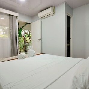 A hotel room with a bed, a door, an air conditioning unit, and a view of greenery outside. - Toucan Arenal Lodge (La Fortuna)