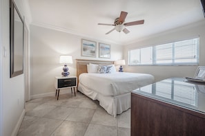 Une chambre à coucher avec un lit, des tables de chevet, un ventilateur de plafond et une fenêtre avec des stores.