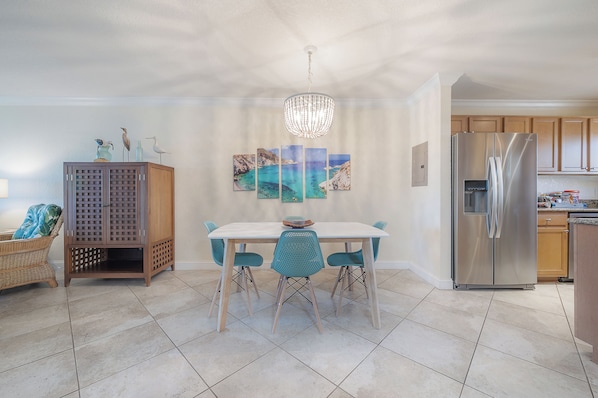 Une cuisine moderne avec une table à manger, des chaises, un lustre et un réfrigérateur.