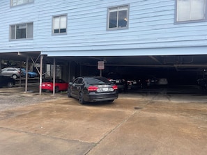 A garage with a black car parked inside, a red car parked outside, and a blue building in the background. - Cozy studio near UT and downtown close to everything! (Austin)