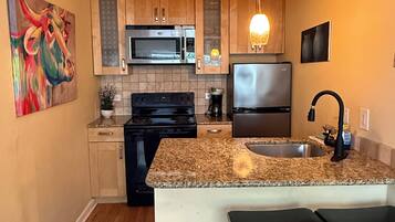 A kitchen with wooden cabinets, a microwave, stove, refrigerator, granite countertop, and two bar stools.