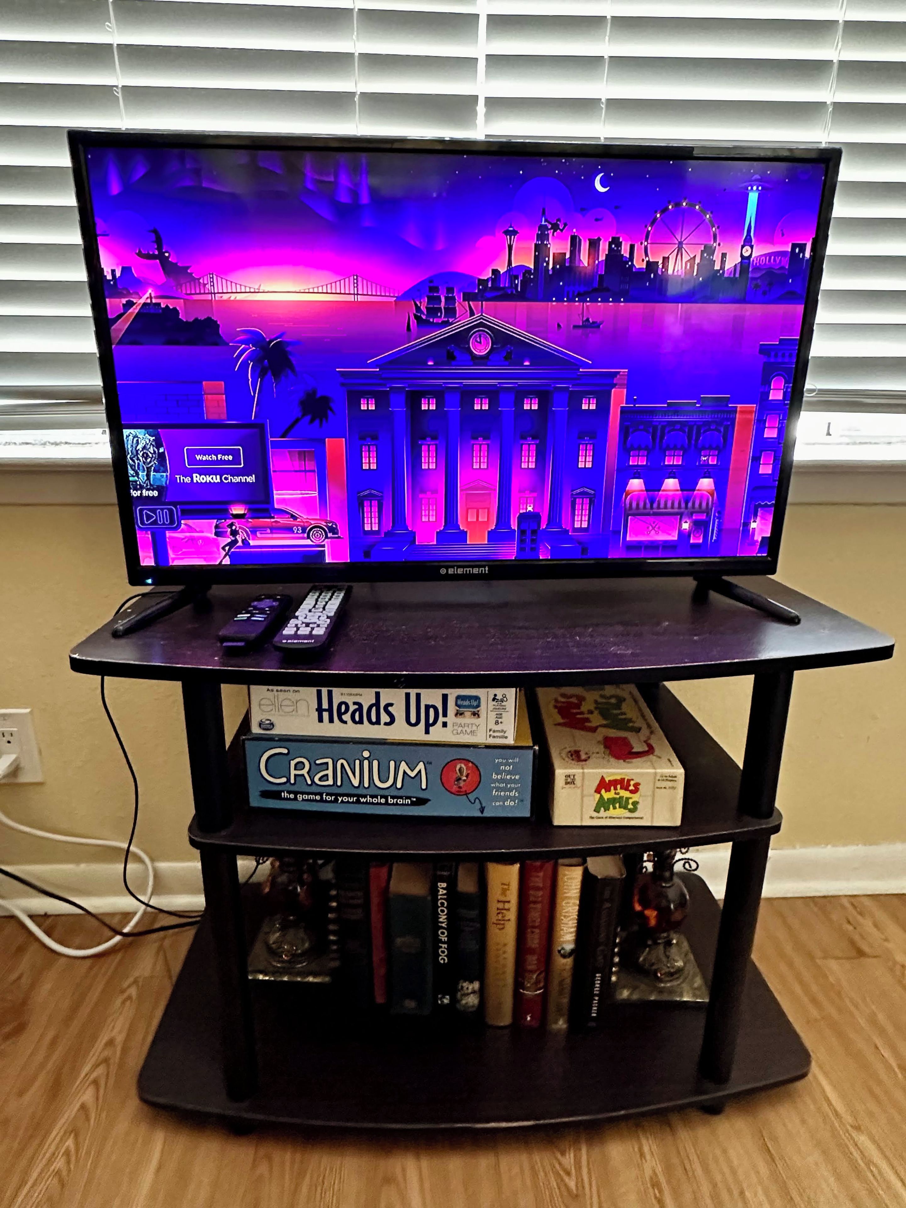 A television on a stand with a cityscape background, a remote control, and board games on the stand.