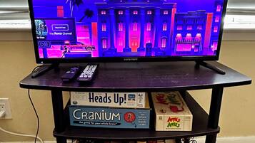 A television on a stand with a cityscape background, a remote control, and board games on the stand.