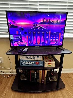 A television on a stand with a cityscape background, a remote control, and board games on the stand.