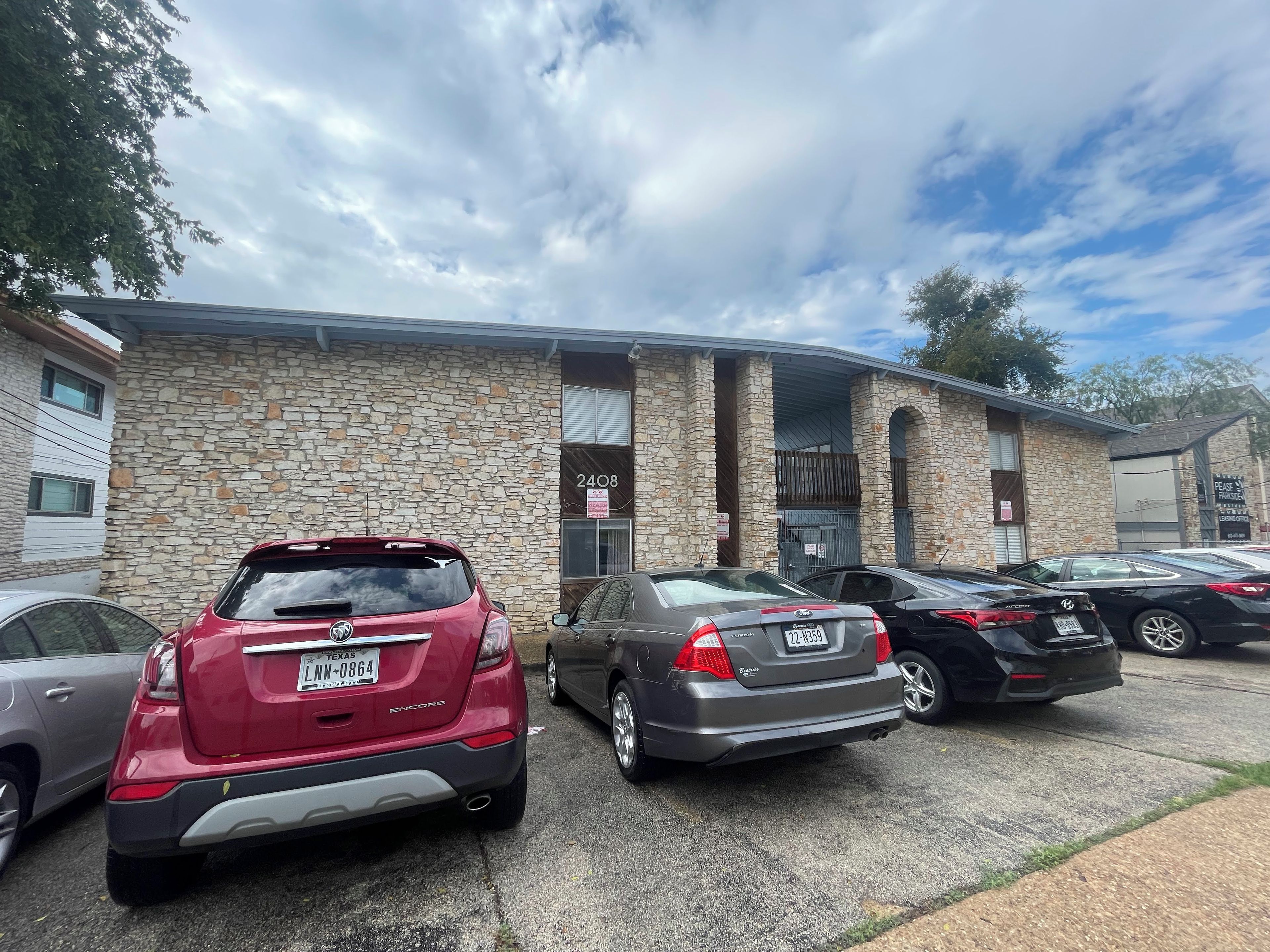A parking lot with several cars parked in front of a building with stone walls and a sign indicating a leasing office.