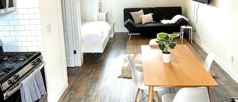 Un espacio habitable compacto con kitchenette, un sofá, una mesa de comedor con sillas y un televisor montado en la pared.