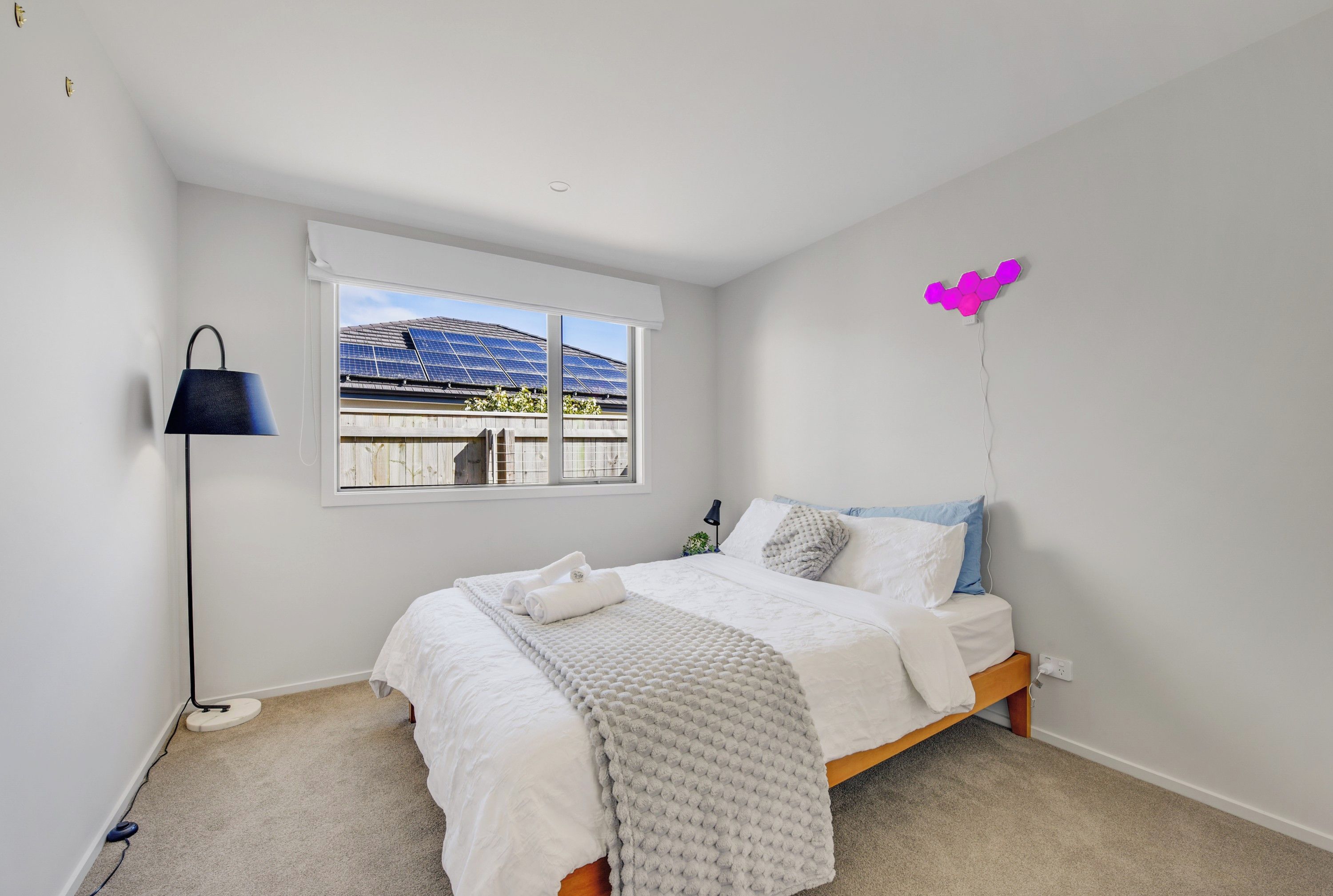A bedroom with a bed, a window with solar panels, a lamp, and a wall-mounted light fixture.
