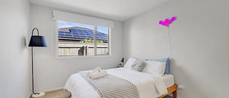 A bedroom with a bed, a window with solar panels, a lamp, and a wall-mounted light fixture.