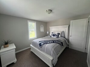 Quarto com uma cama, mesa de cabeceira, janela e porta.