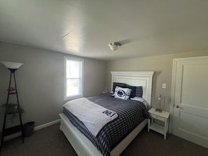 Ein Schlafzimmer mit Bett, Nachttisch, Lampe, Fenster und Tür.