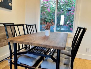 A dining table with chairs, a vase with flowers, and a window with a view of pink flowers.