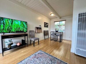 A room with a television, a chair, a small table, a rug, and a window with blinds.