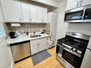 A kitchen with white cabinets, a stainless steel stove, a microwave, and a tiled backsplash.