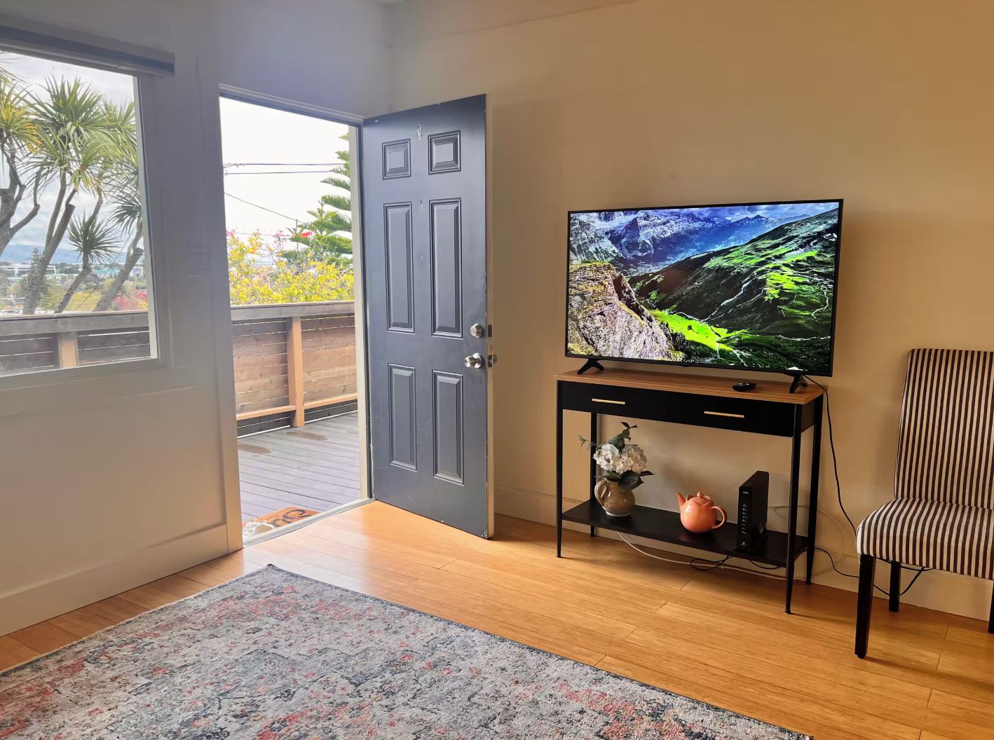 Una habitación con una televisión sobre un mueble bajo, una puerta que da a un espacio exterior y una silla a rayas.