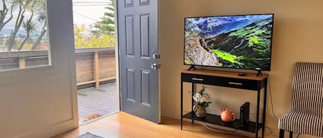 A room with a television on a stand, a door leading to an outdoor area, and a striped chair.