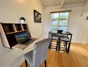 A modern room with a laptop on a shelf, a dining table with chairs, and a window with a view of greenery.