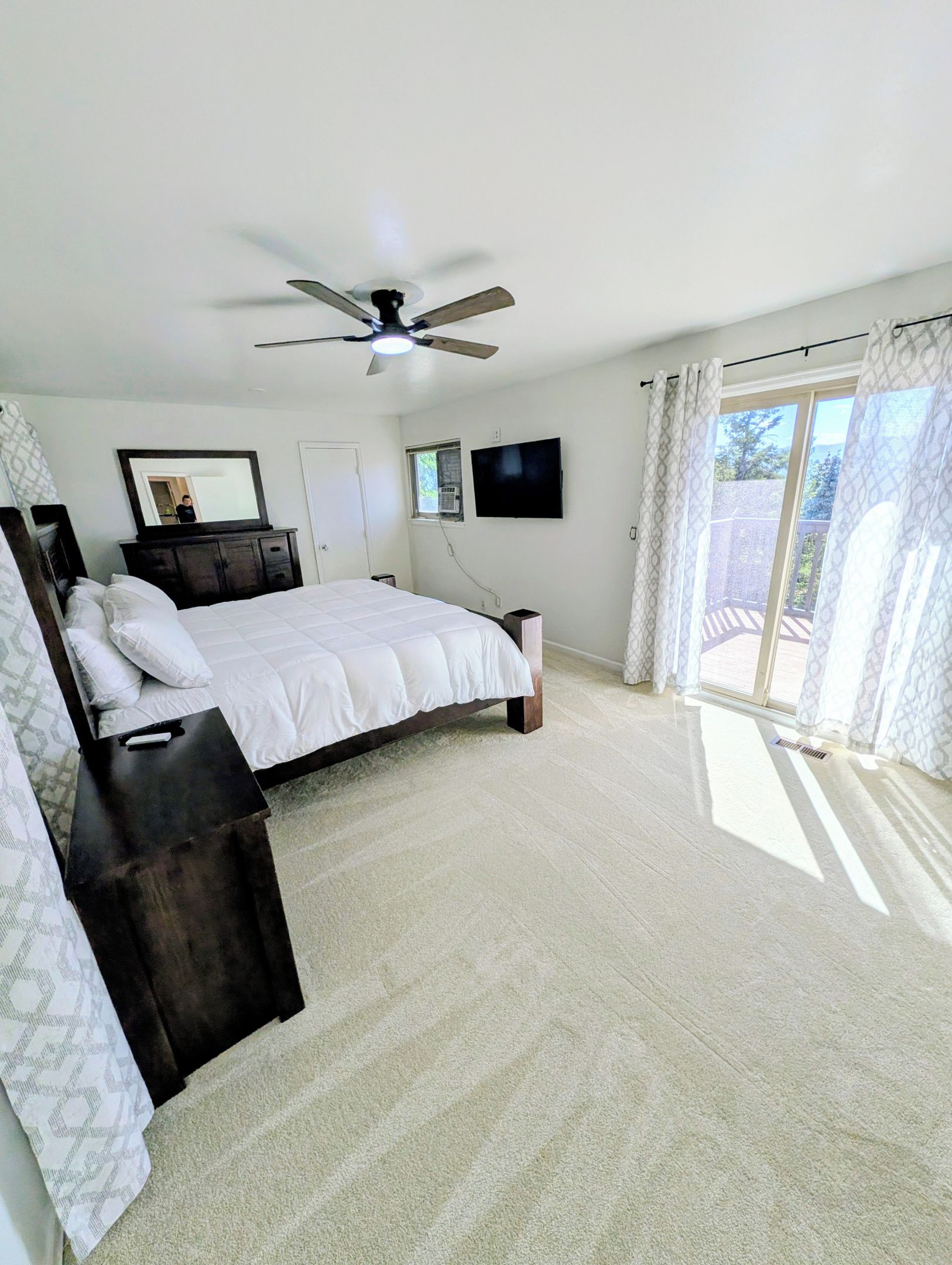 Une chambre à coucher avec un lit, un ventilateur de plafond, une télévision et une fenêtre avec des rideaux.
